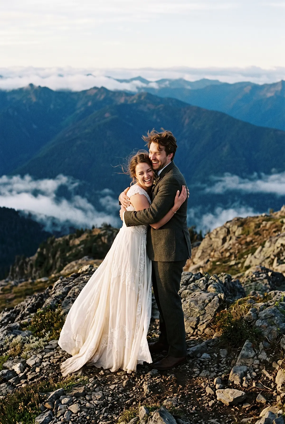 A bride and groom embracing on a rocky mountain summit at sunrise after their vows.