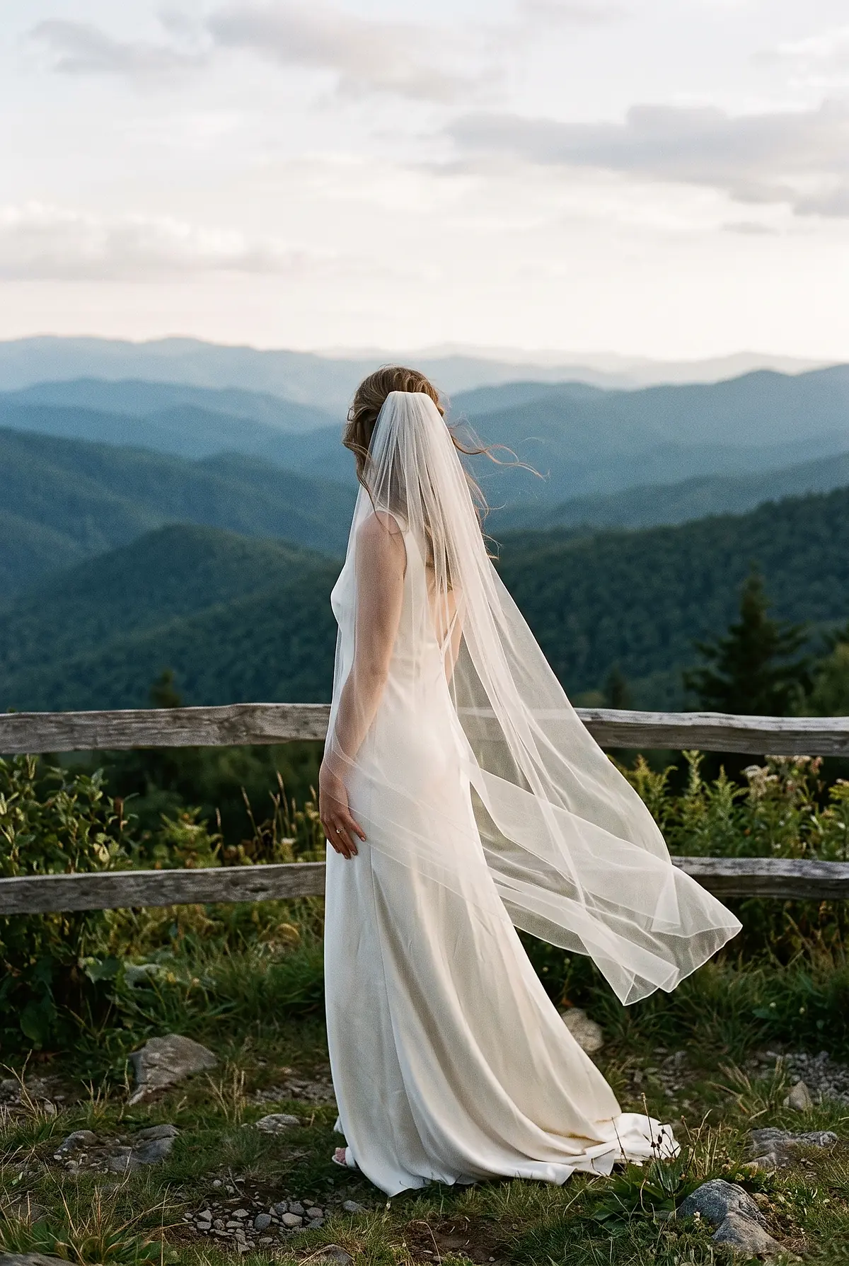A bride standing at a mountain overlook with her veil lifting in the wind.