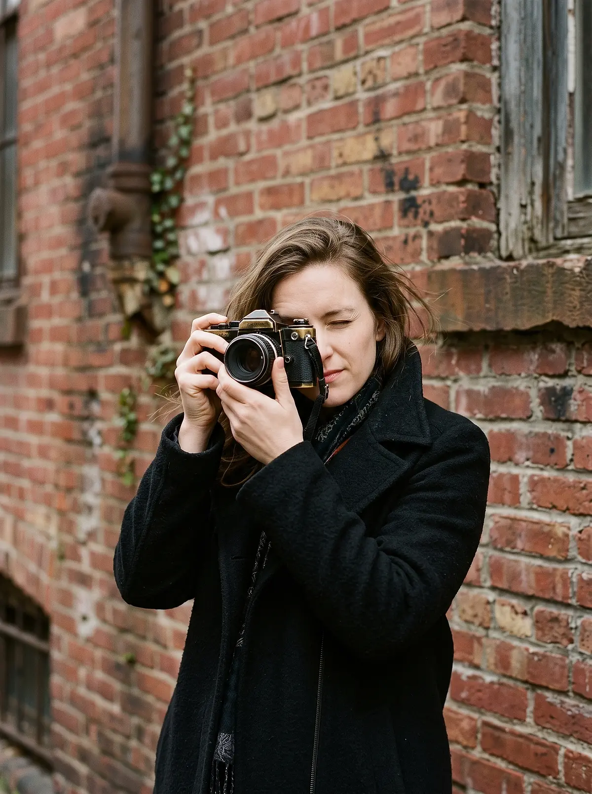 Ondine Reyes holding a film camera to her eye, standing against a brick wall in Brooklyn.