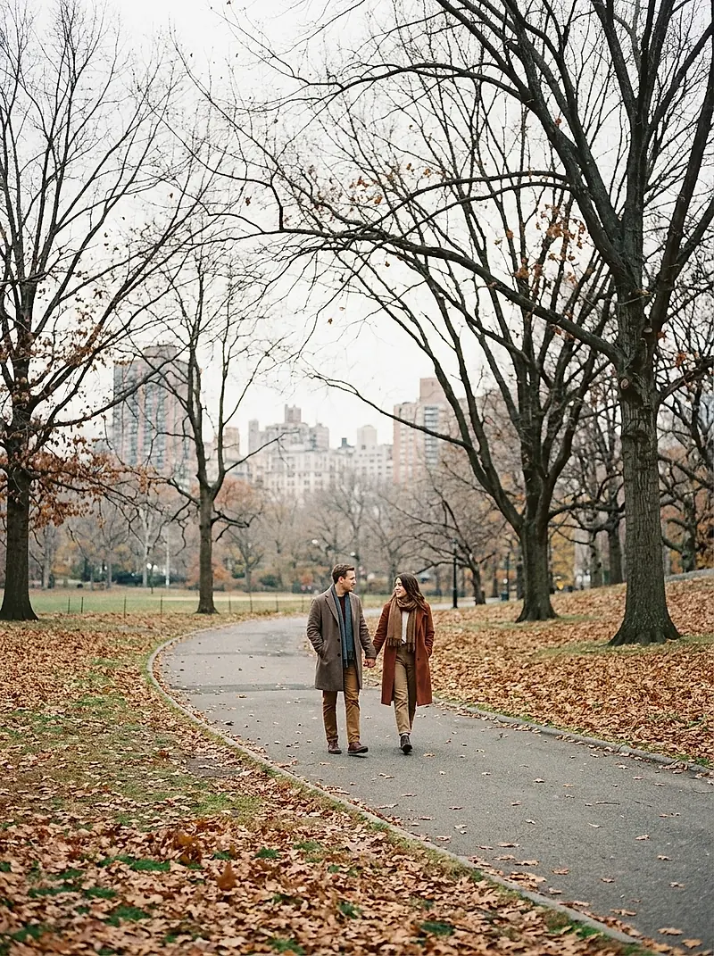 A couple walking hand in hand along a late-autumn park path.