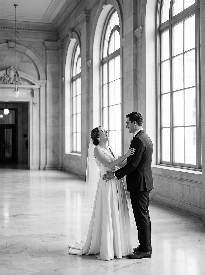 A bride and groom laughing together in the hallway of a city hall.