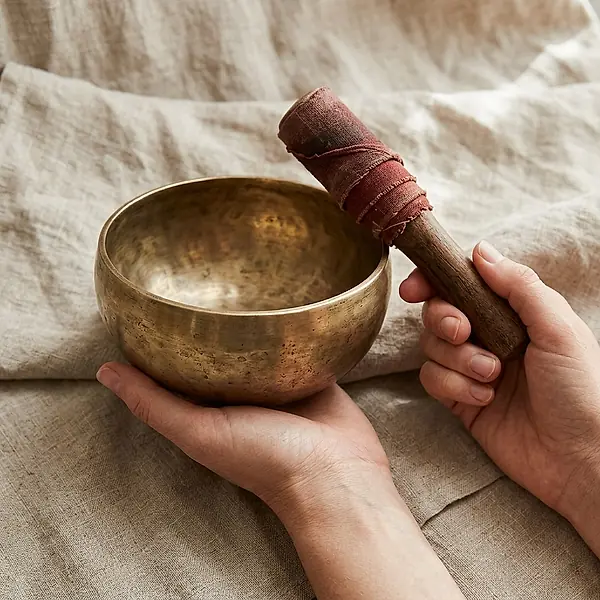Hands hold a singing bowl and a wooden mallet.