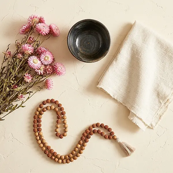 Dried pink flowers, a small bowl and a folded cloth on a cream surface.