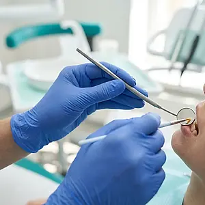 A dentist's gloved hands holding a dental mirror during a check-up.