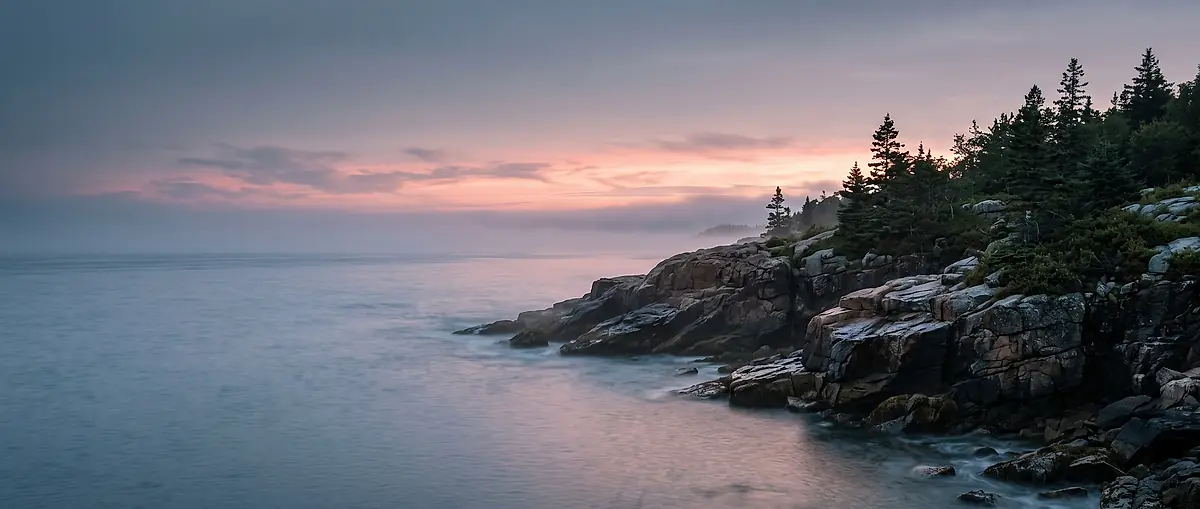 The Maine coast at dusk, granite headland and calm water under a pink sky
