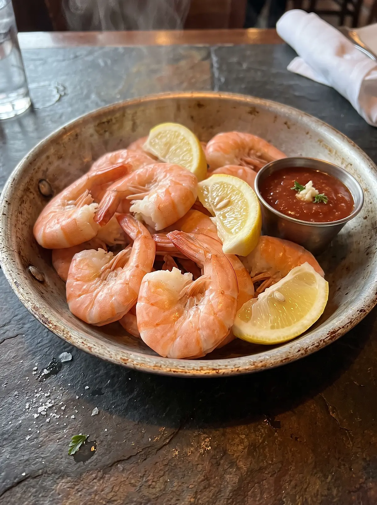 A pan of hot steamed shrimp with lemon wedges and a cup of cocktail sauce