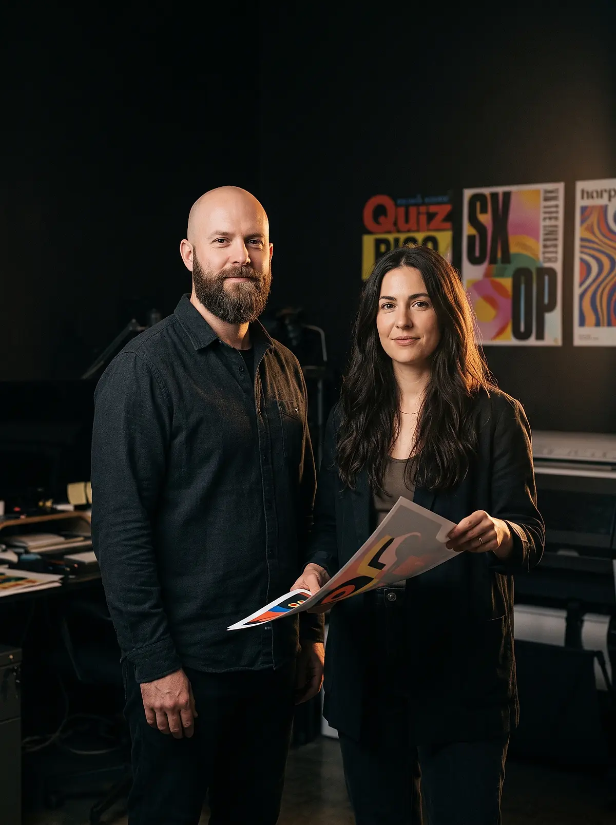 The two designers behind Big Loud Studio standing side by side in their Austin studio, holding a freshly printed sheet.