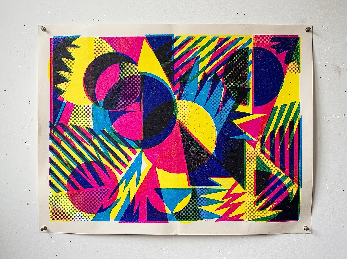 A screen printed gig poster in loud geometric colours pinned to a studio wall.