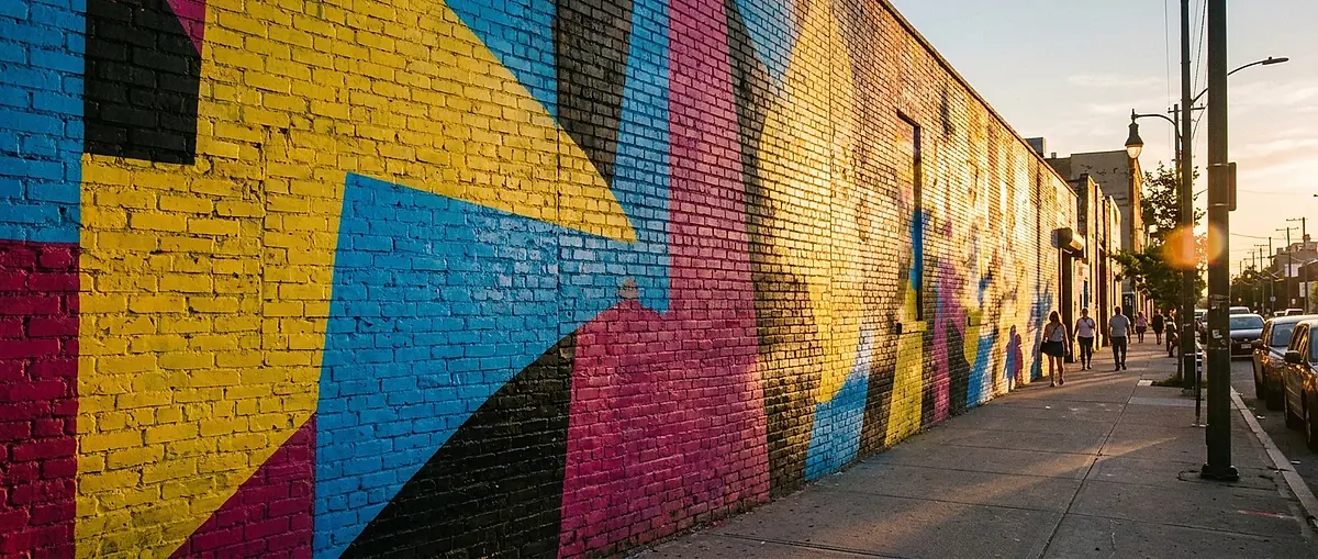 A full wall mural in bold geometric colours painted on a brick wall along a city street.