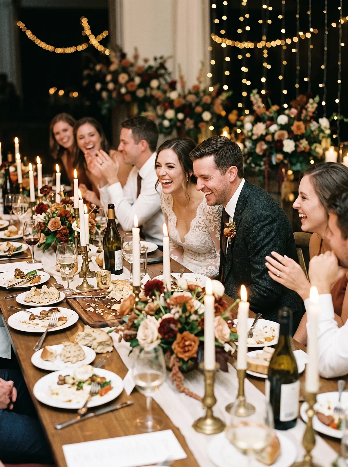 A bride and groom laughing with guests at a candlelit reception table