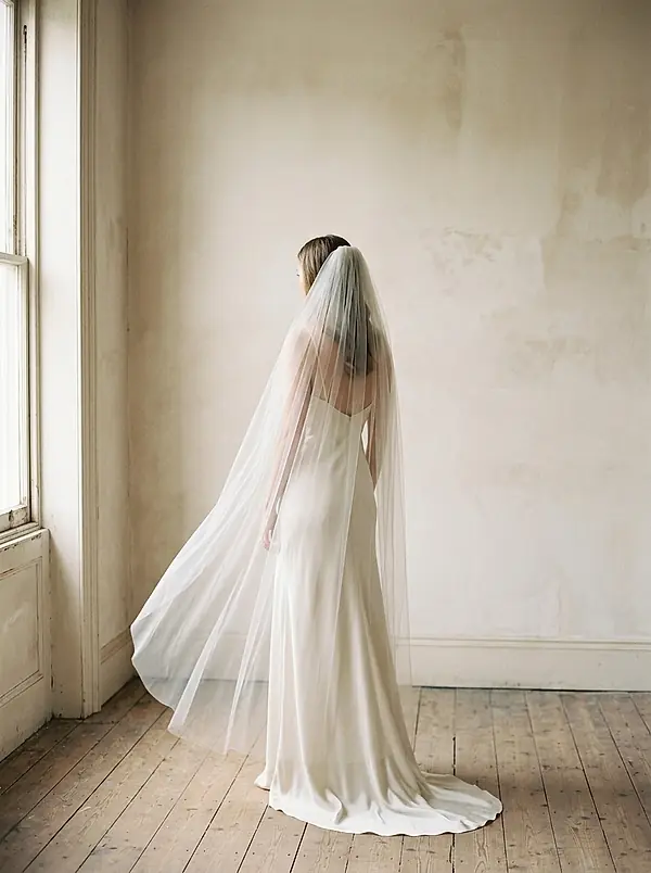 A bride in an ivory gown seen from behind in soft window light