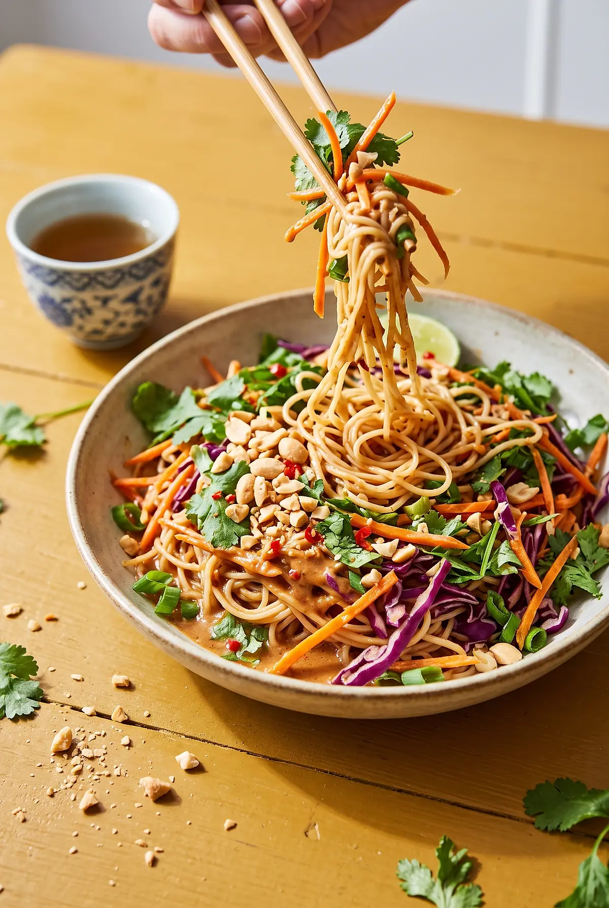 Chopsticks lifting noodles from a bowl of Thai peanut noodle salad