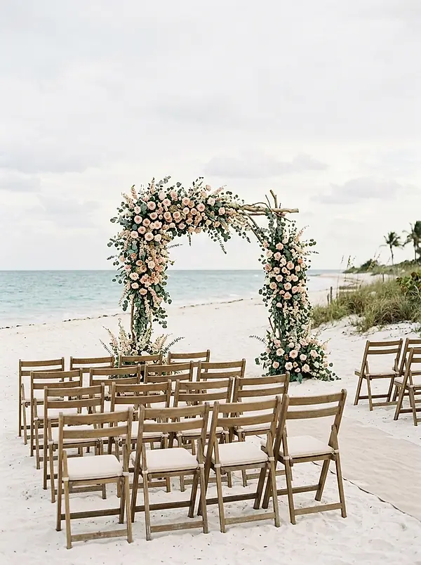 A floral arch and chairs set up for a ceremony on white sand