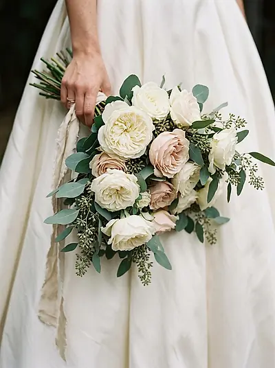 A bride holding a bouquet of white and blush roses