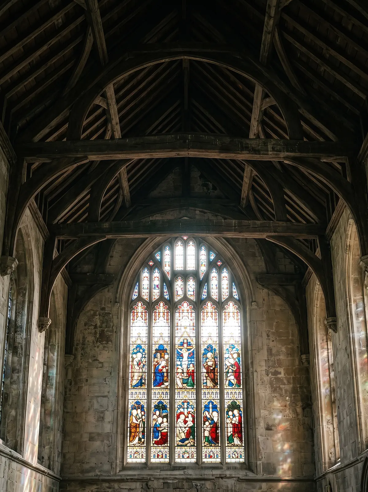 A tall stained glass window above the dark timber roof trusses of the church