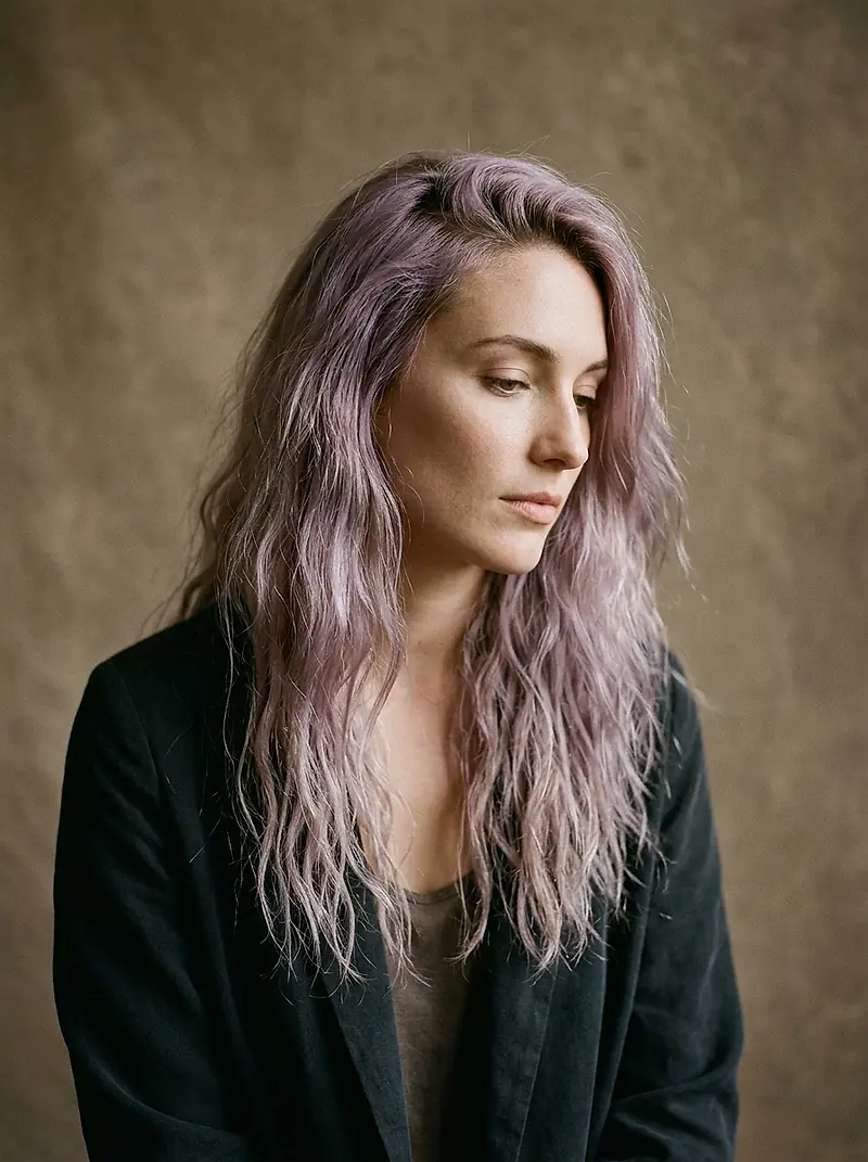 A stylist with long lilac-tinted waves, looking away from the camera.
