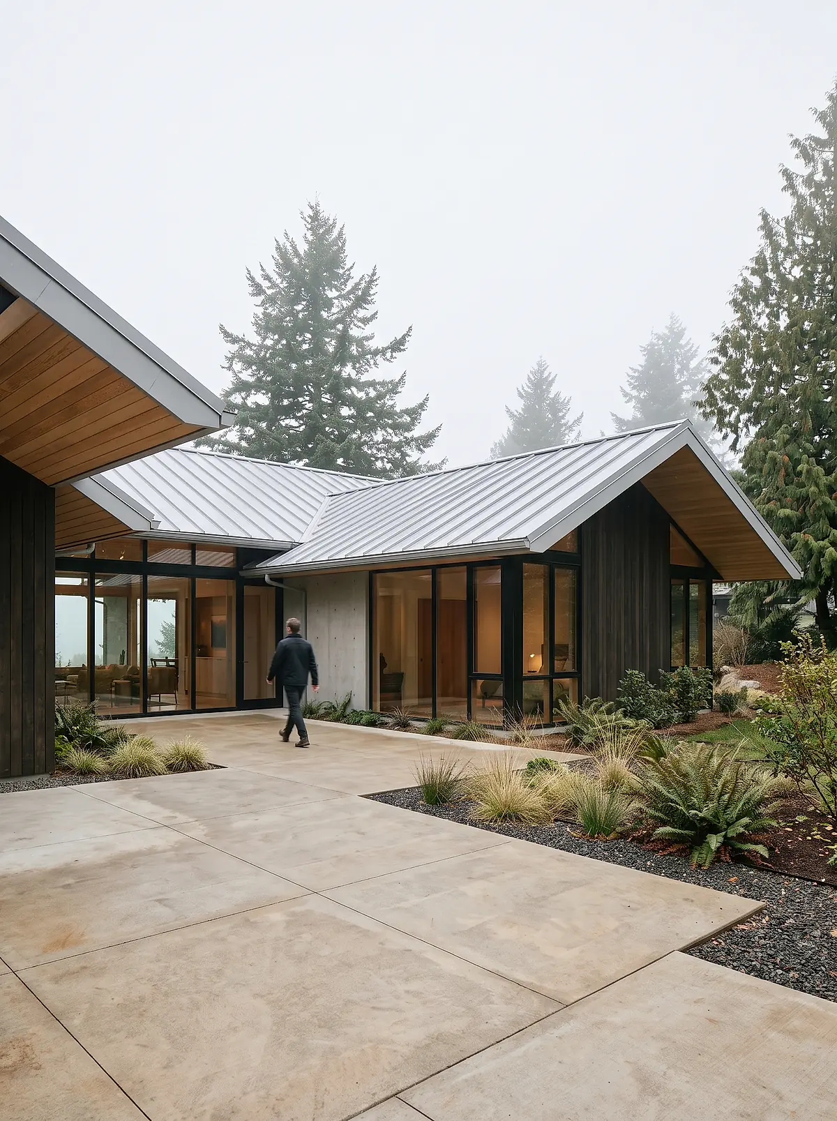 A person walking across the courtyard of a single storey home with a light grey standing seam metal roof.