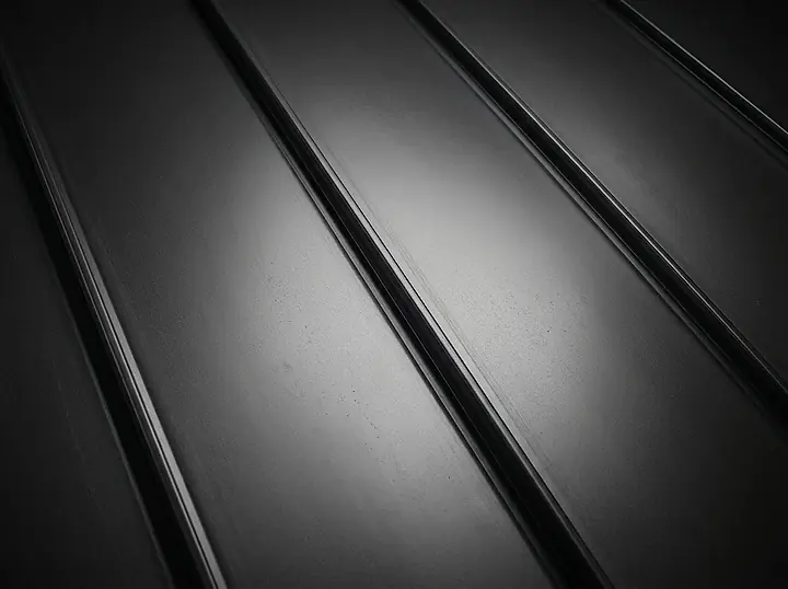 Close view of charcoal standing seam panels with light raking across the metal.