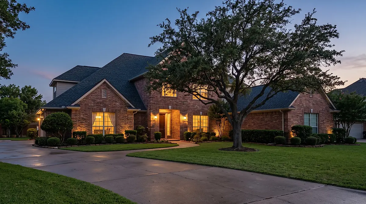 A two storey brick home with a new shingle roof photographed at dusk, interior lights on.