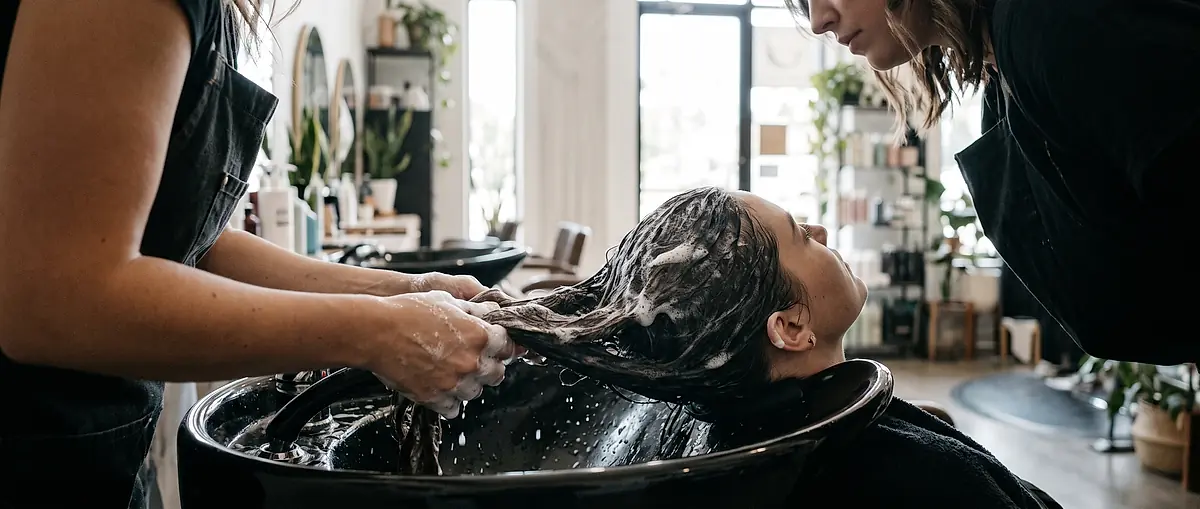 Hands working shampoo through a client's wet hair at the wash basin