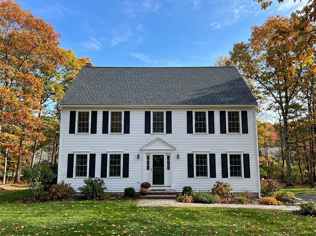 A white New England colonial house with a newly finished dark shingle roof.
